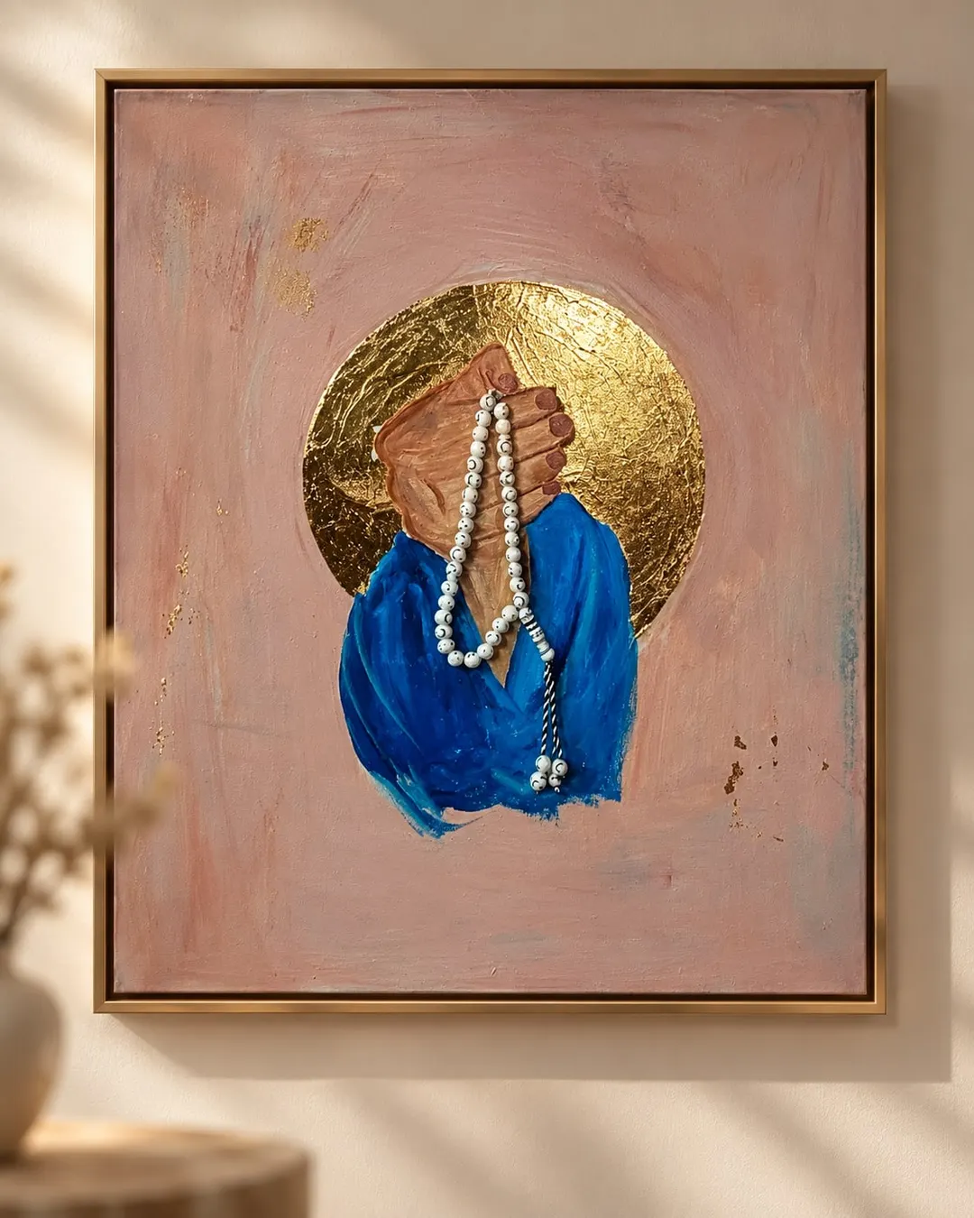 Tasbih (Where Hearts Find Rest), a painting by Hafsa Imran in a gold frame: two clasped hands holding a string of white prayer beads, in blue sleeves, before a circle of gold on a dusty pink ground flecked with gold