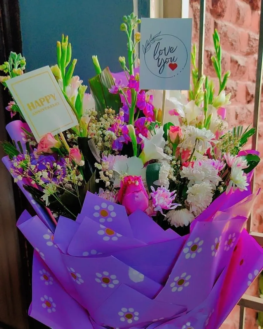 A vibrant purple-wrapped bouquet with mixed flowers and a handwritten 'Happy Anniversary' card — handcrafted by Bloom & Beyond in Lahore