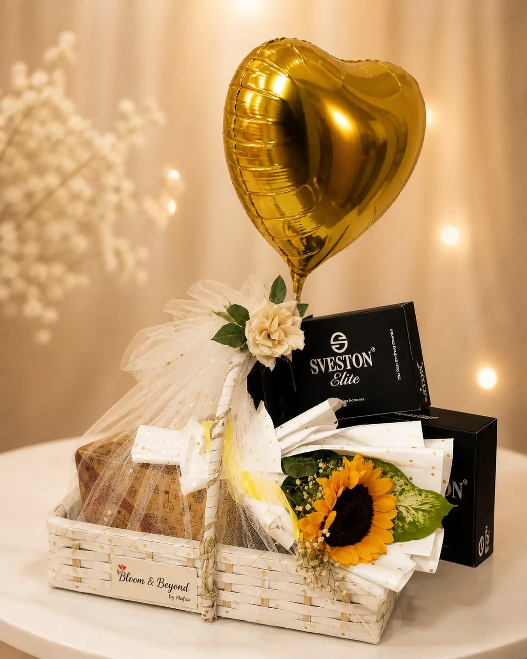 An empty handwoven wicker gift frame in cream tulle with fresh sunflower and rose accents, baby breath and a gold heart balloon — handcrafted by Bloom & Beyond in Lahore