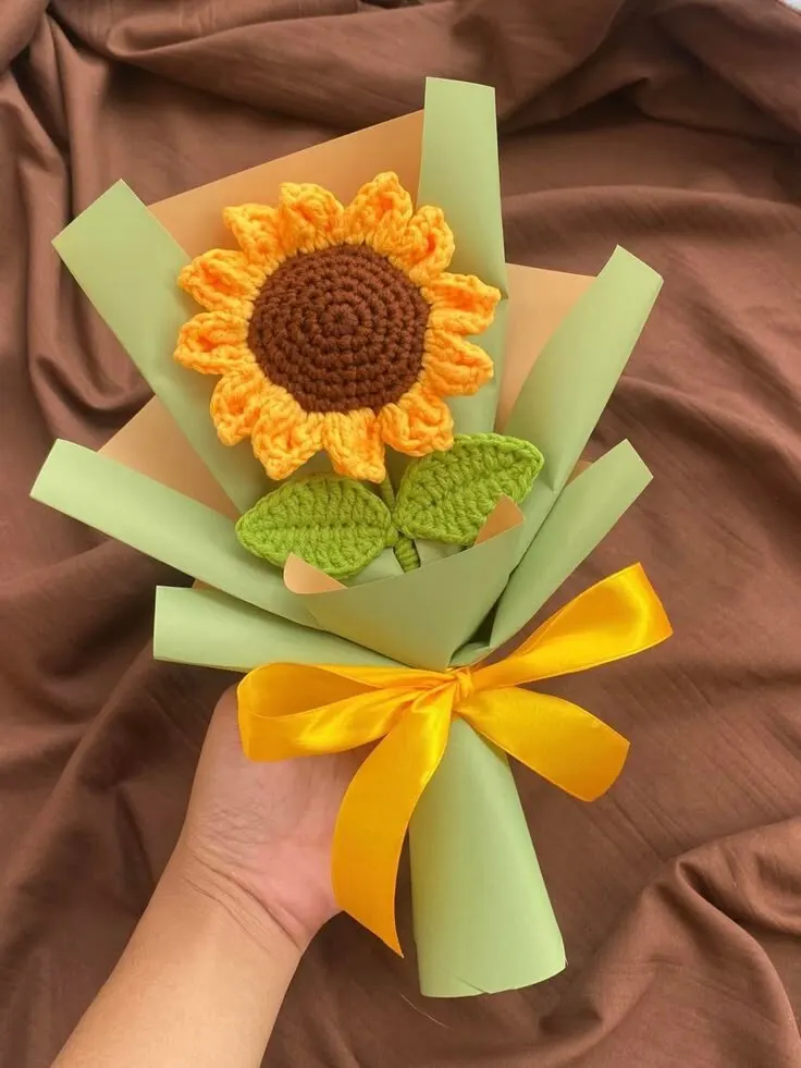A hand-crocheted yellow sunflower on a single stem wrapped in sage green paper with a yellow satin bow — handcrafted by Bloom & Beyond in Lahore