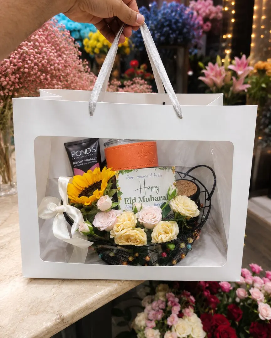 A presentation gift bag holds a small basket of sunflowers and cream roses, a Pond's skincare treat, chocolates — handcrafted by Bloom & Beyond in Lahore