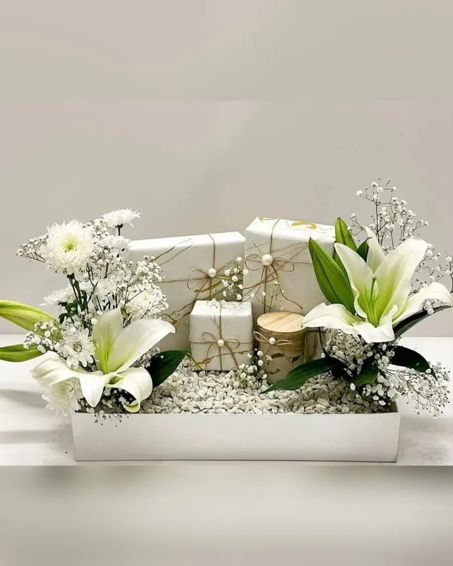 An elegant gift tray with white lilies, chrysanthemums, baby breath, wrapped gifts, and a scented candle — handcrafted by Bloom & Beyond in Lahore