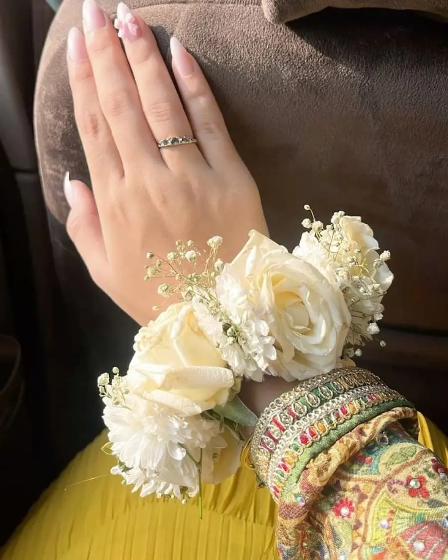 A delicate white rose wrist corsage worn over mehndi-adorned hands — handcrafted by Bloom & Beyond in Lahore
