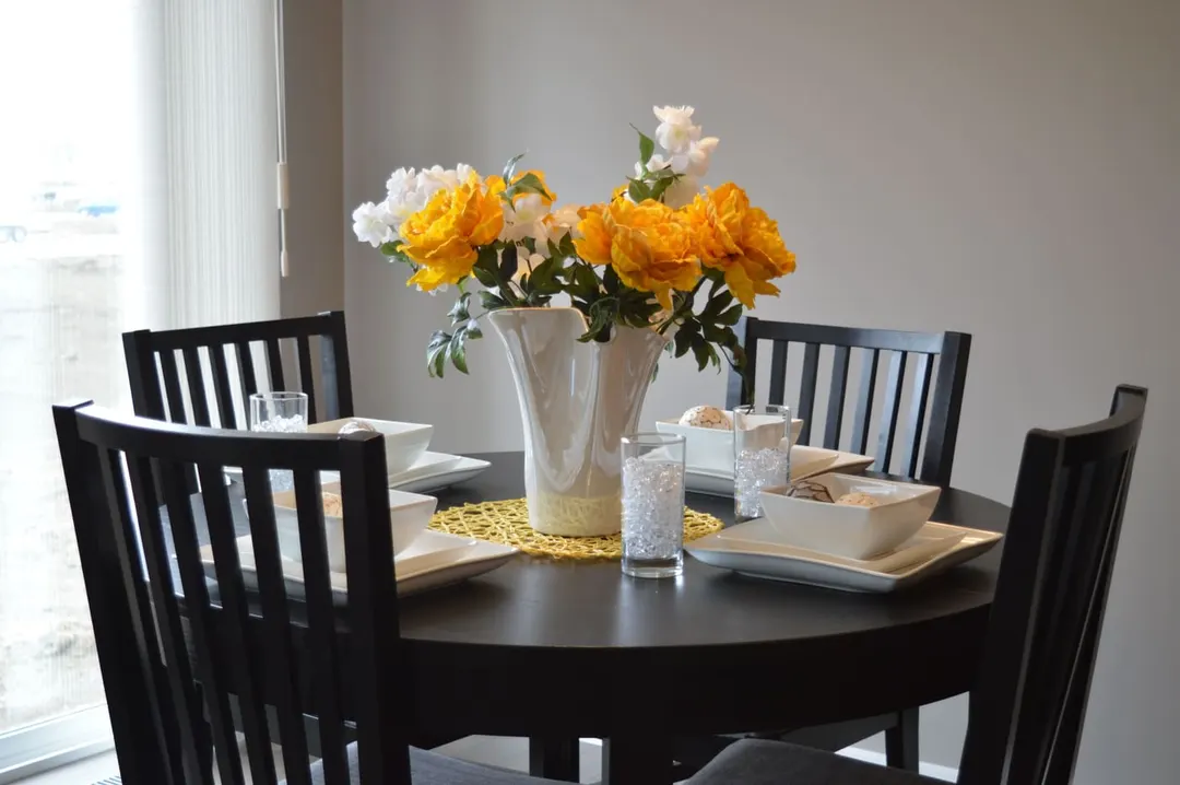 Orange and white roses in a white vase at the centre of a round dining table