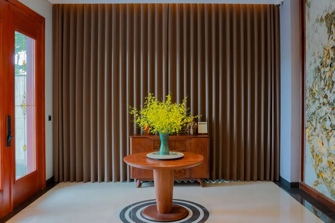 Yellow orchids in a teal vase on a round wooden table in a home entrance