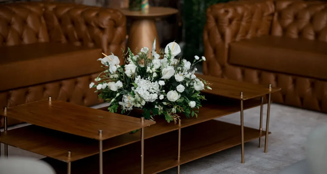 Low white flower arrangement on a wooden coffee table between two leather sofas