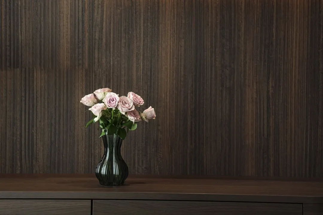 Pale pink roses in a dark glass vase on a walnut cabinet against wood panelling
