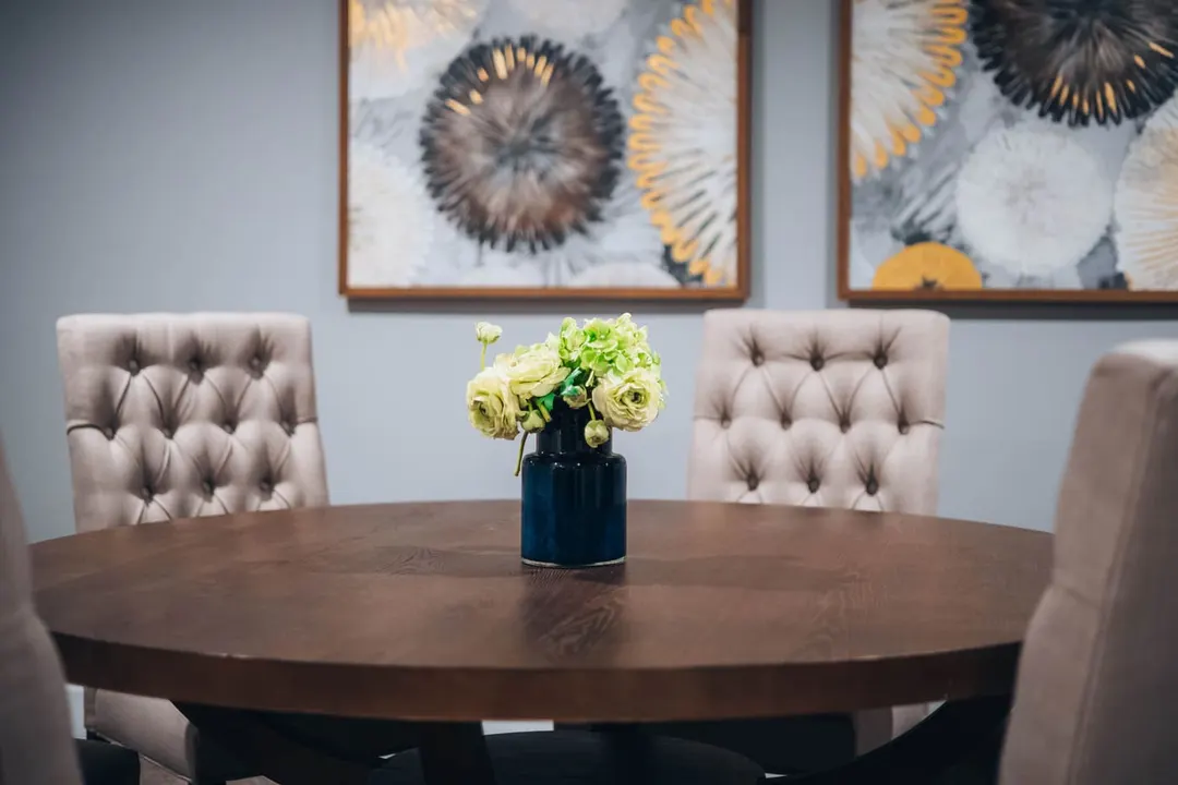 White and green flowers in a navy vase on a round meeting table with upholstered chairs