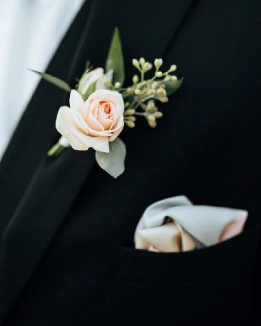 A boutonniere featuring a blush rose with baby breath and greenery, pinned on the lapel — handcrafted by Bloom & Beyond in Lahore