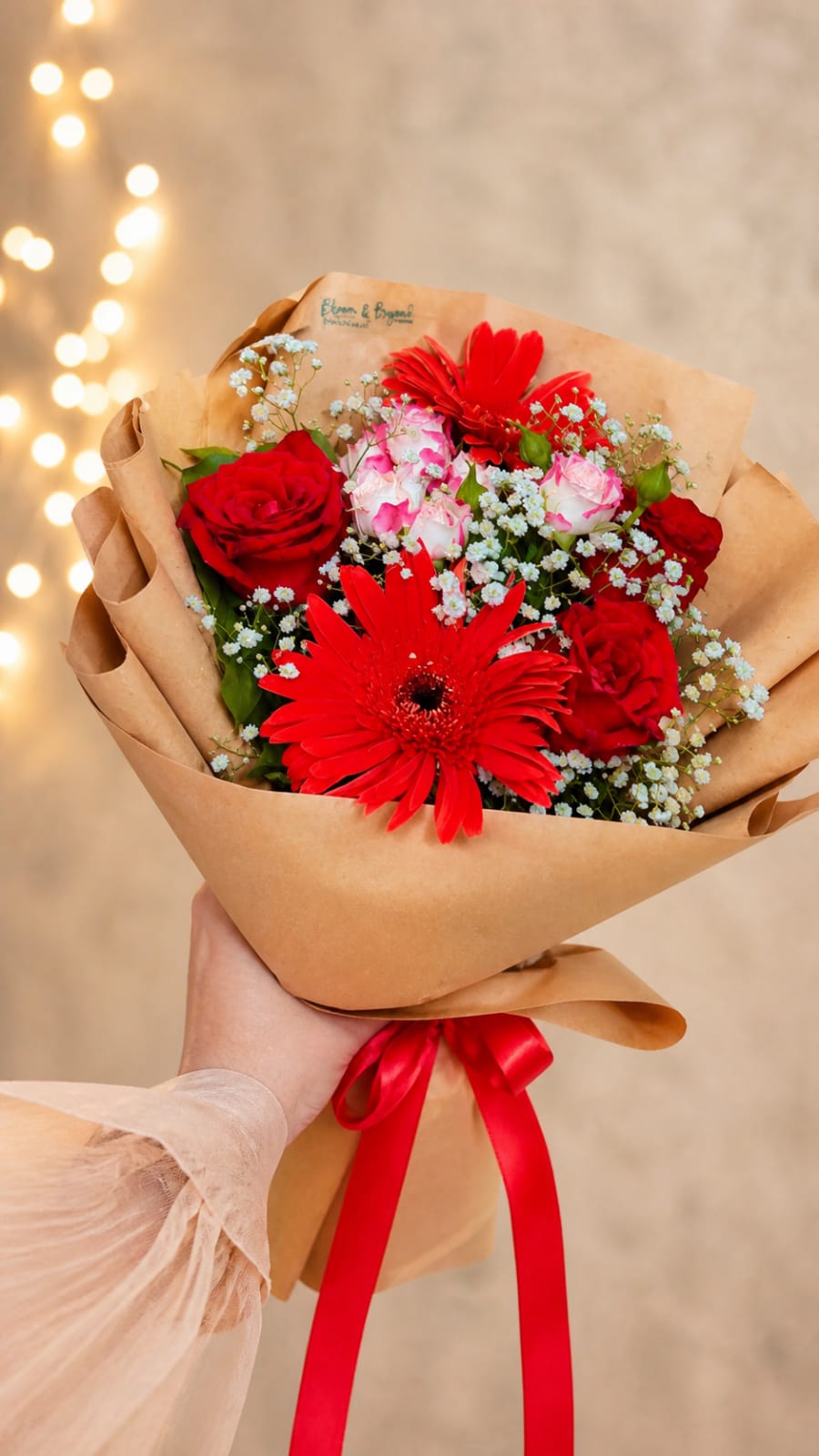 Mixed flower bouquet of red roses, red gerbera daisies, cream roses and baby's breath, hand-tied in kraft paper with a red satin ribbon — handcrafted by Bloom & Beyond in Lahore