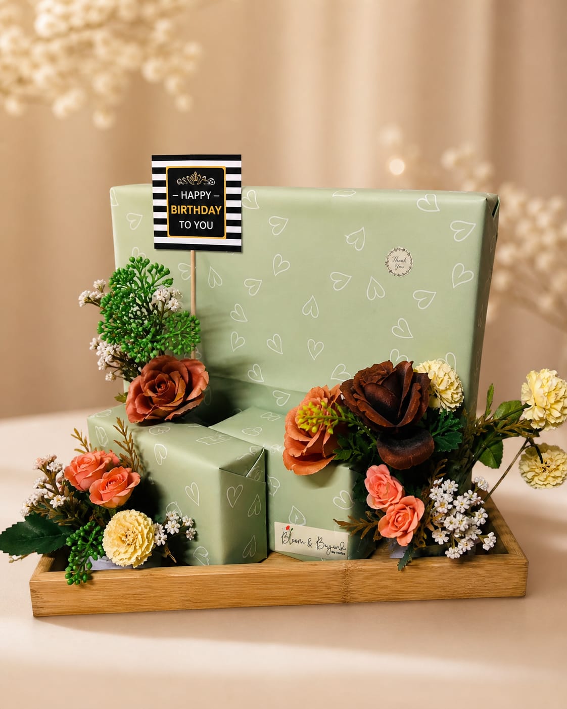 Birthday gift hamper with flowers — three sage-green gift boxes on a bamboo tray with roses, carnations and white wildflowers — handcrafted by Bloom & Beyond in Lahore