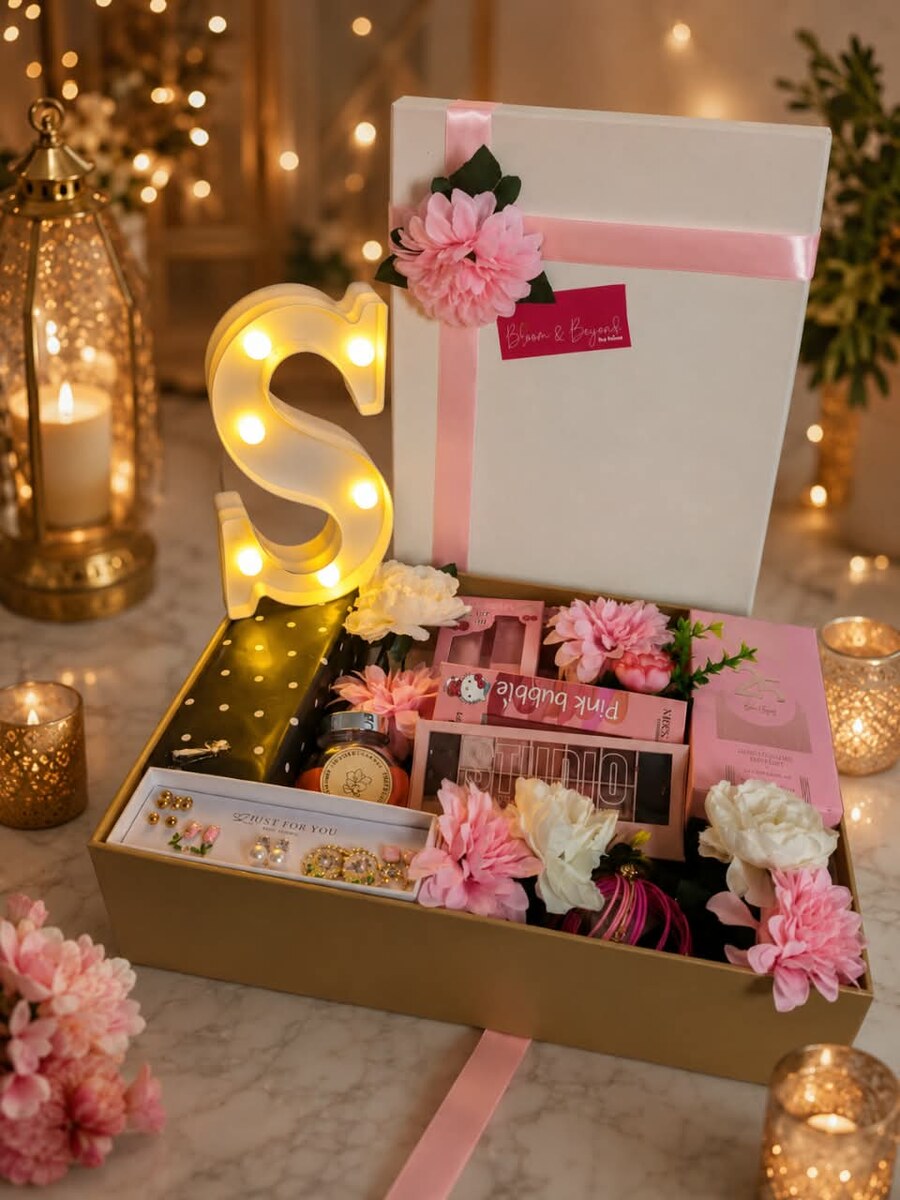 A gold gift box with a lit marquee initial letter, pink flowers and a curated set of beauty products — handcrafted by Bloom & Beyond in Lahore