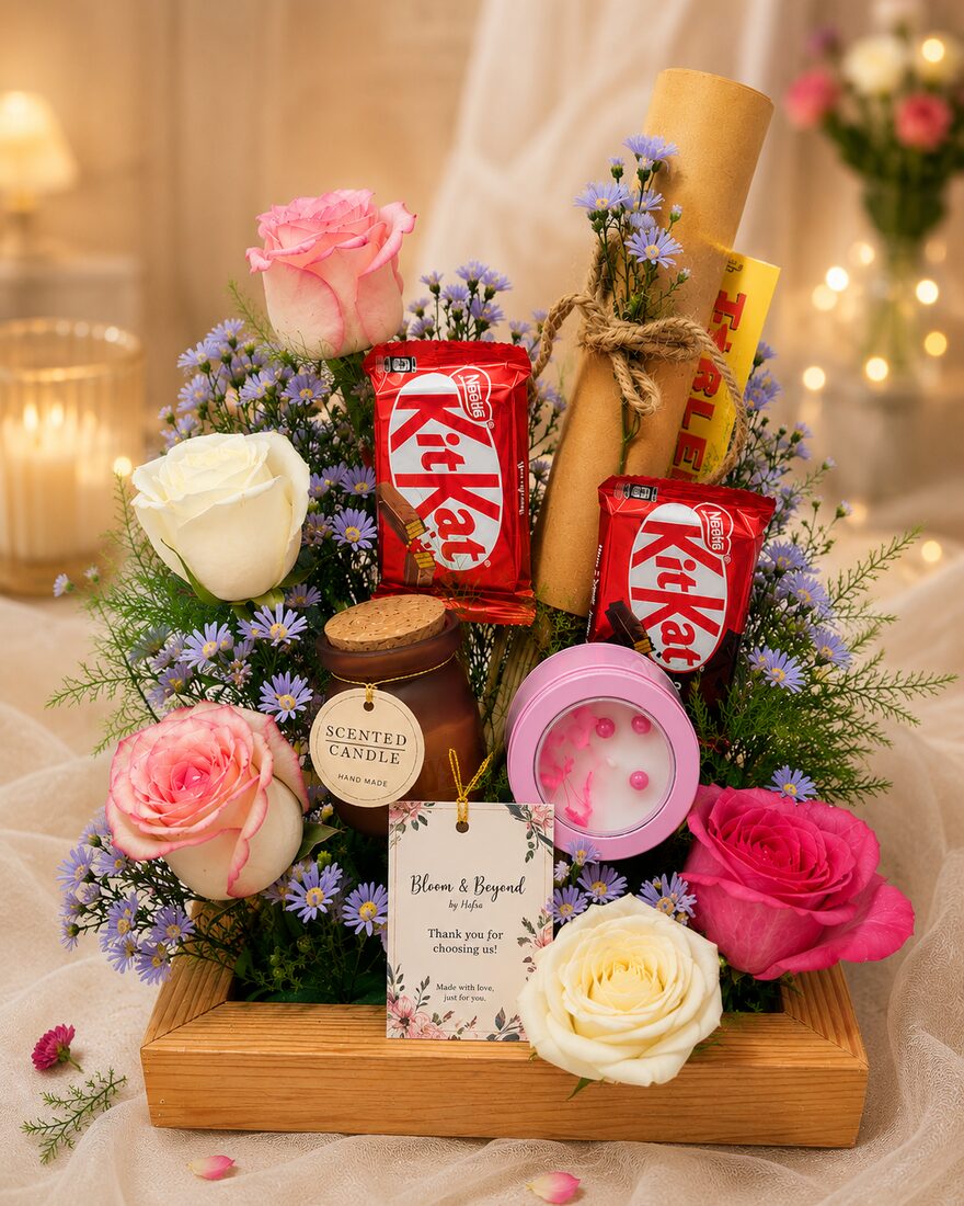A wooden keepsake tray of fresh pink, white and cream roses with blue aster filler, arranged around KitKat bars — handcrafted by Bloom & Beyond in Lahore